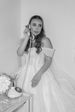 A bride in a classic white ball gown poses with a vintage telephone in black and white.