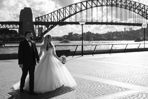Sydney Harbour Bridge provides dramatic backdrop for wedding photoshoot on waterfront promenade.