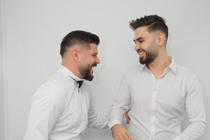 Two men in white shirts share a lighthearted moment against a white background.