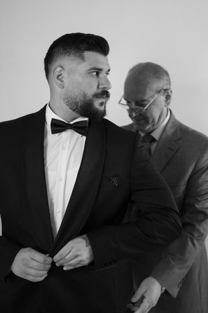 A formal black and white portrait of two men in suits preparing for an event.
