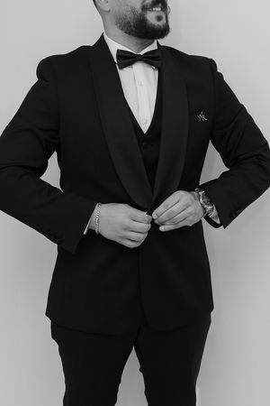 Black and white photo of groom adjusting his tuxedo jacket.