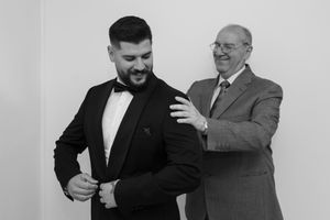 Two men share a candid moment while getting ready in formal attire.