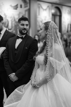 Black and white wedding portrait showing bride in an elaborate veil and gown during ceremony.