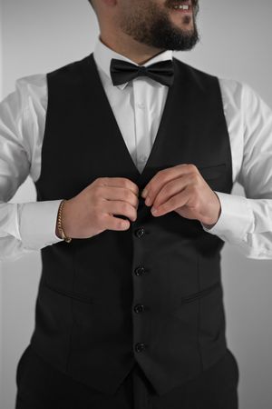 Detail shot of hands buttoning a formal black vest over a white dress shirt.