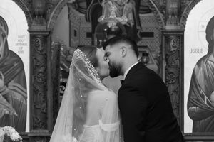 Intimate black and white wedding kiss photo captured between religious iconography in church.