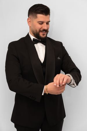 Groom checking his watch while wearing classic black tuxedo and bow tie.