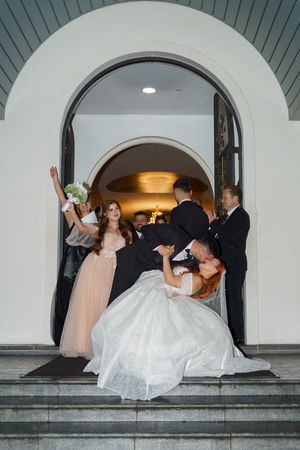 Wedding party poses dramatically on church steps with bride being dipped for photo.