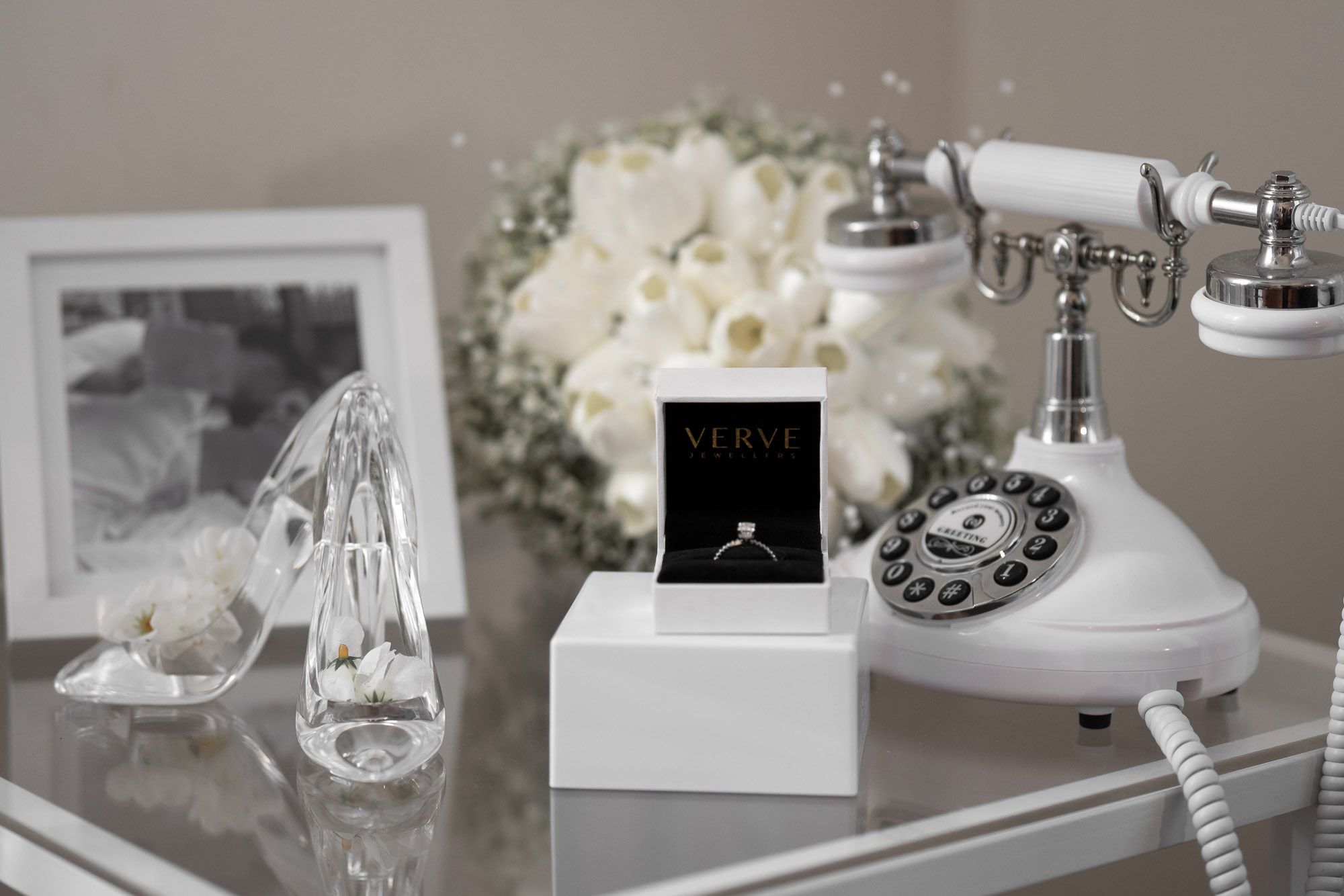 Wedding detail flatlay with perfume bottles, jewelry and white floral arrangements.