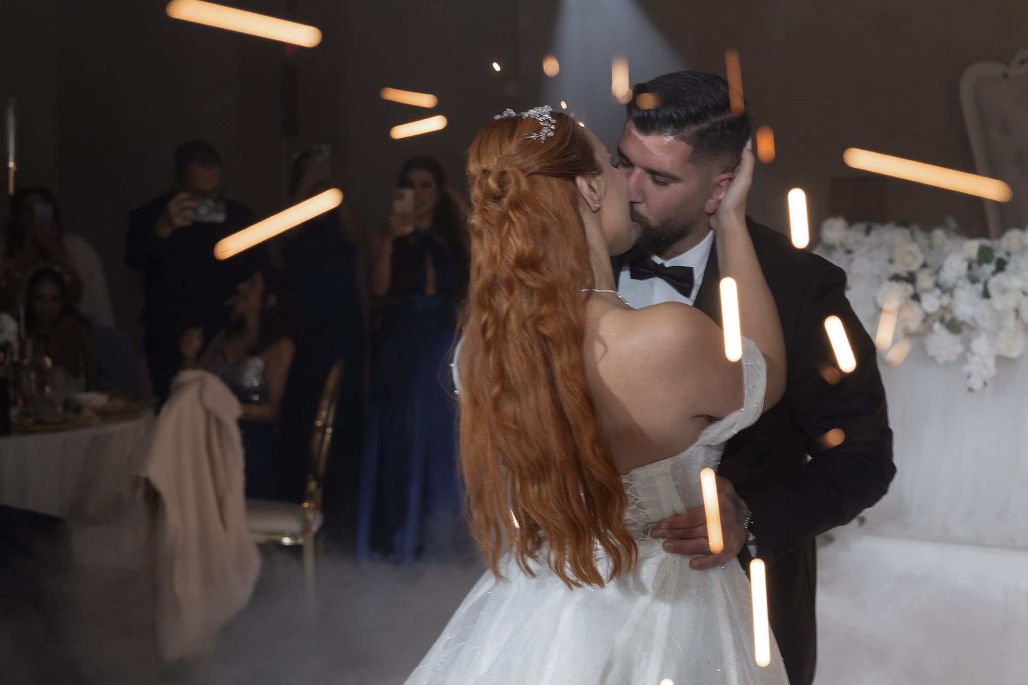 Dancing couple embraces during romantic moment at dimly lit wedding reception.