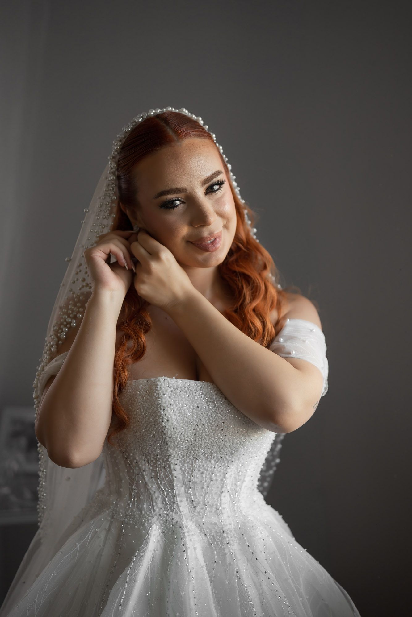 A bride wearing a sparkling white ball gown and veil poses against a dark background.