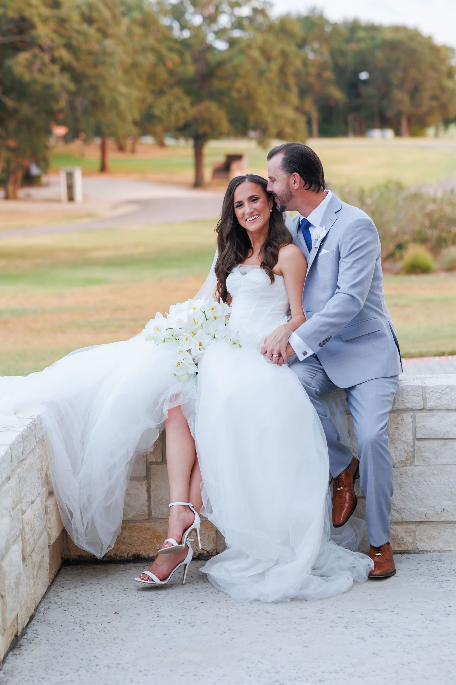 Joyful couple in wedding attire sharing a playful moment at sunset on the lawn at Bella Cavalli