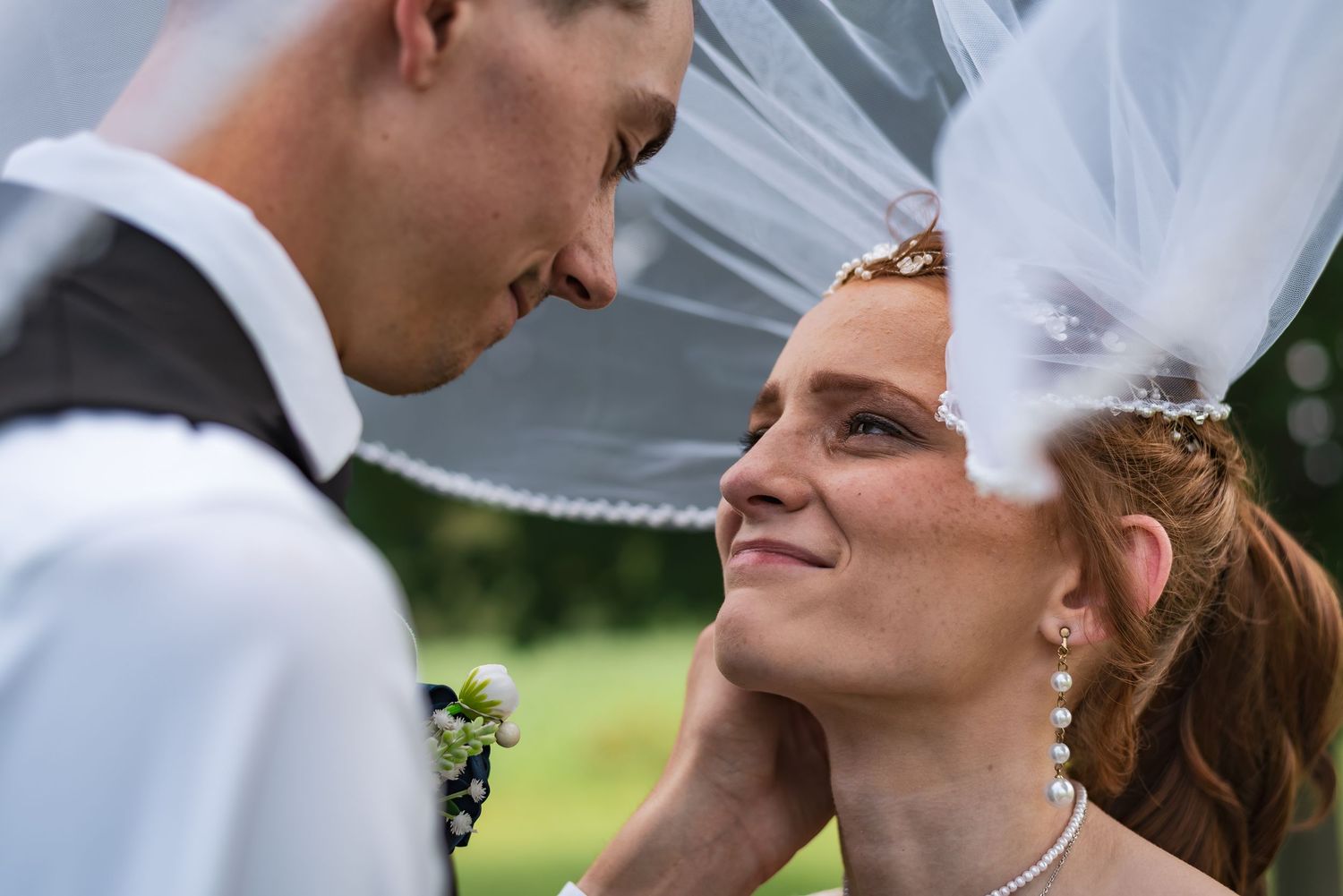Romantic close-up of a couple under a flowing white veil in an outdoor setting.