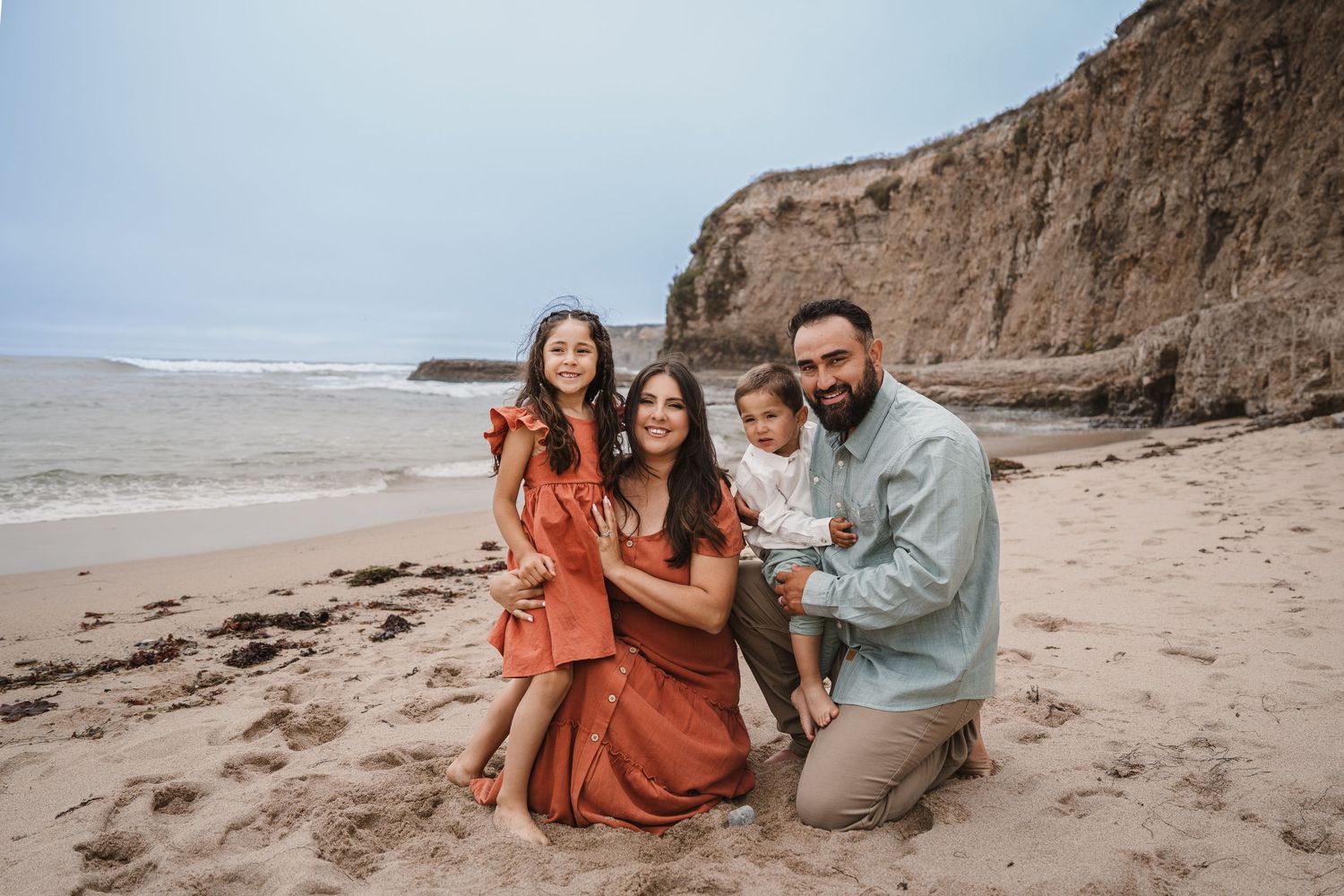 A group poses together on a sandy beach with dramatic cliffs in the background on an overcast day.