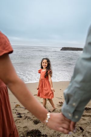 A series of candid beach photos showing someone in a coral dress spinning and walking along the sandy shore.