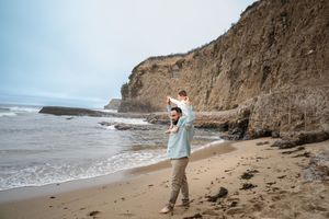 Person enjoying a coastal walk along a sandy beach with dramatic cliffs and crashing waves in the background.