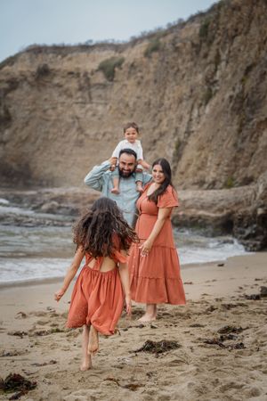 A family enjoys a peaceful moment together on a sandy beach with dramatic cliffs in the background.