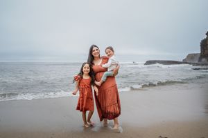 People in matching rust-colored outfits walk along a misty beach with cliffs in the background.