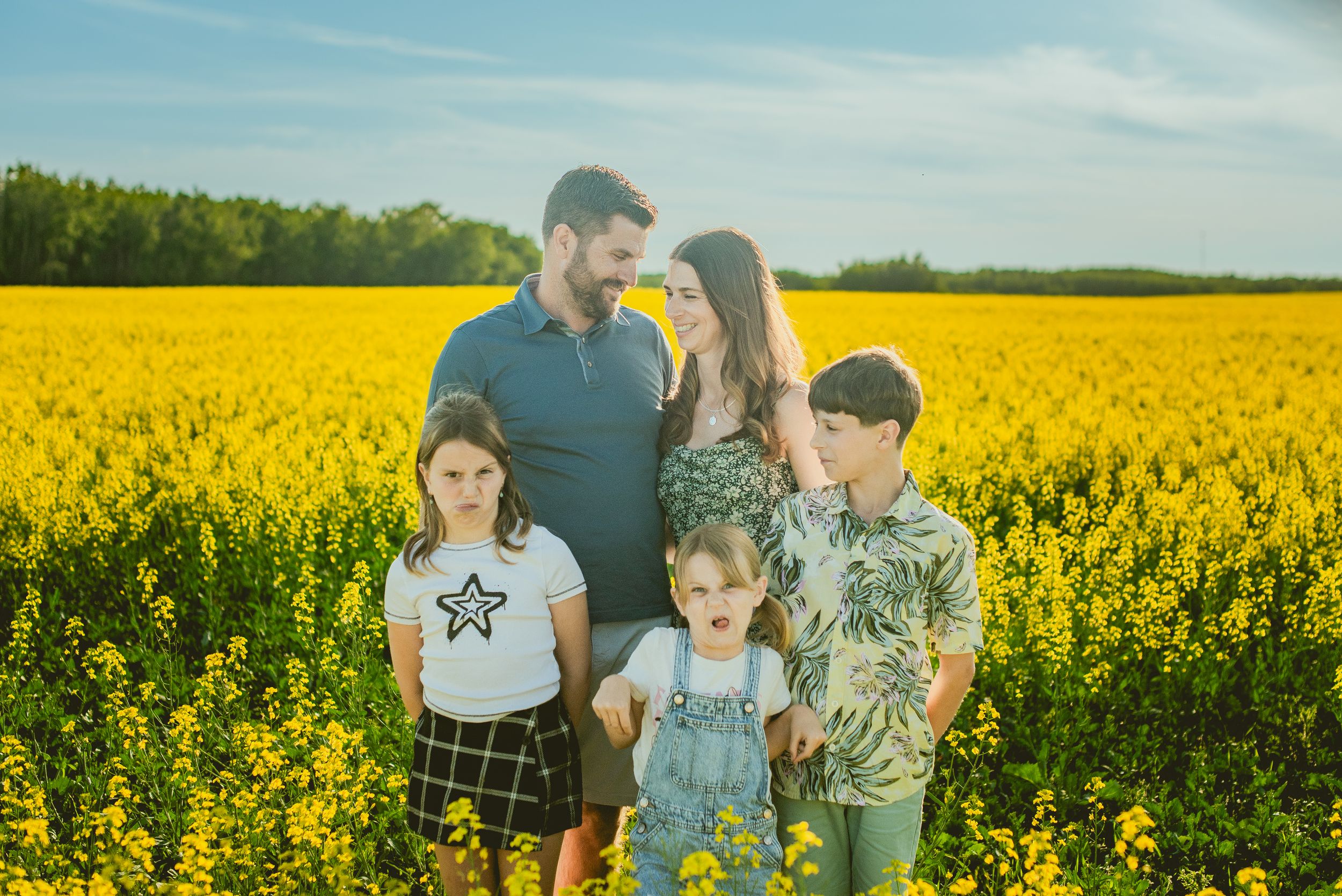 A family enjoys a sunny day in a vibrant yellow canola field during springtime bloom.