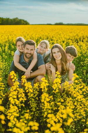 A joyful family lying in a vibrant yellow canola field on a sunny day.