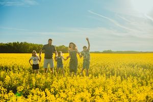 Silhouetted figures stand together with raised arms against a vibrant yellow canola field at sunset.