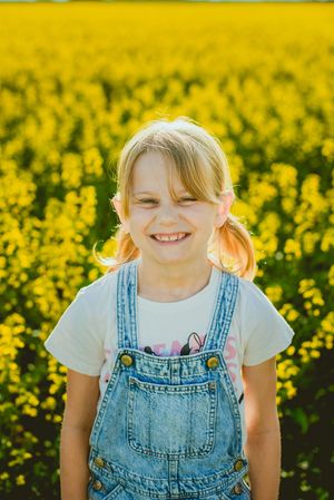 A close-up progression of smiles in bright denim overalls among yellow canola flowers.