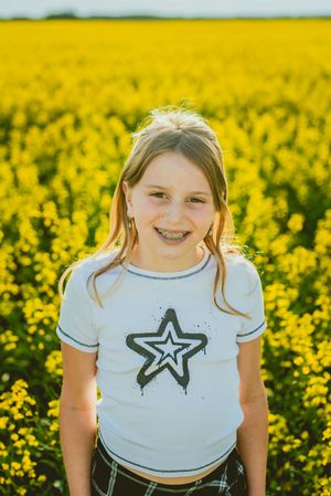 A child in a white t-shirt with star design poses in a bright yellow flowering canola field.