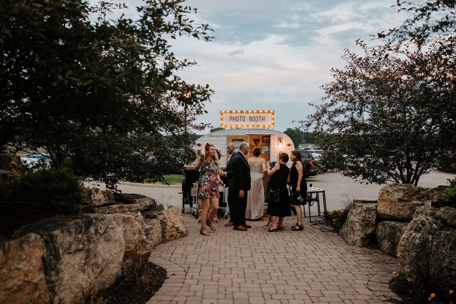 Wedding ceremony gathering at stone archway entrance during sunset.