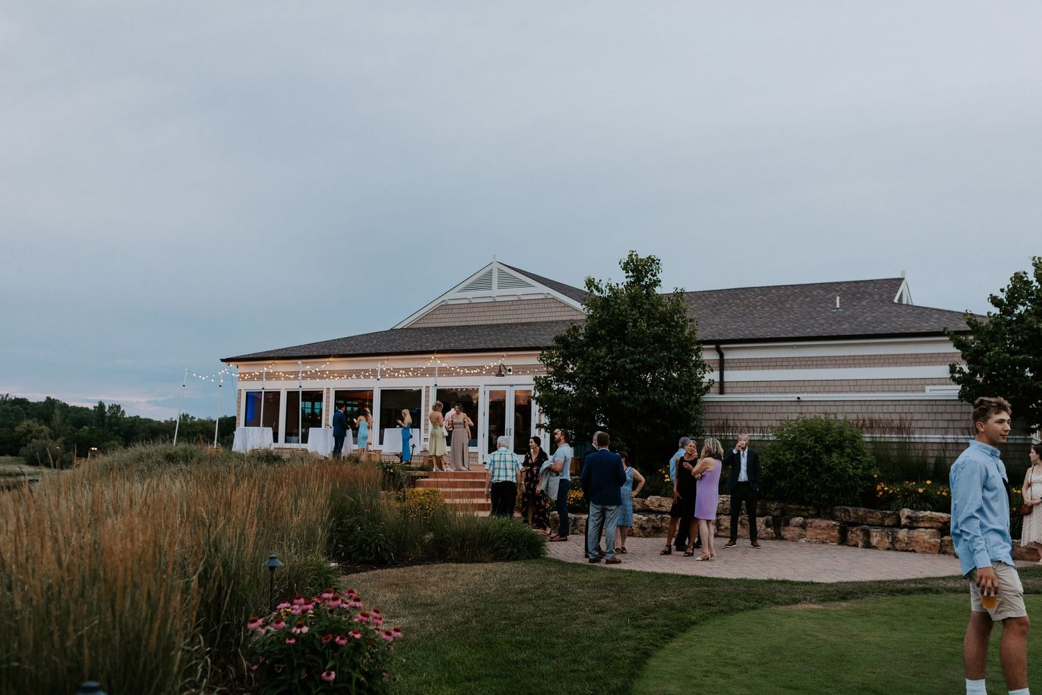 Wedding venue exterior with white pillars and guests on patio at dusk.