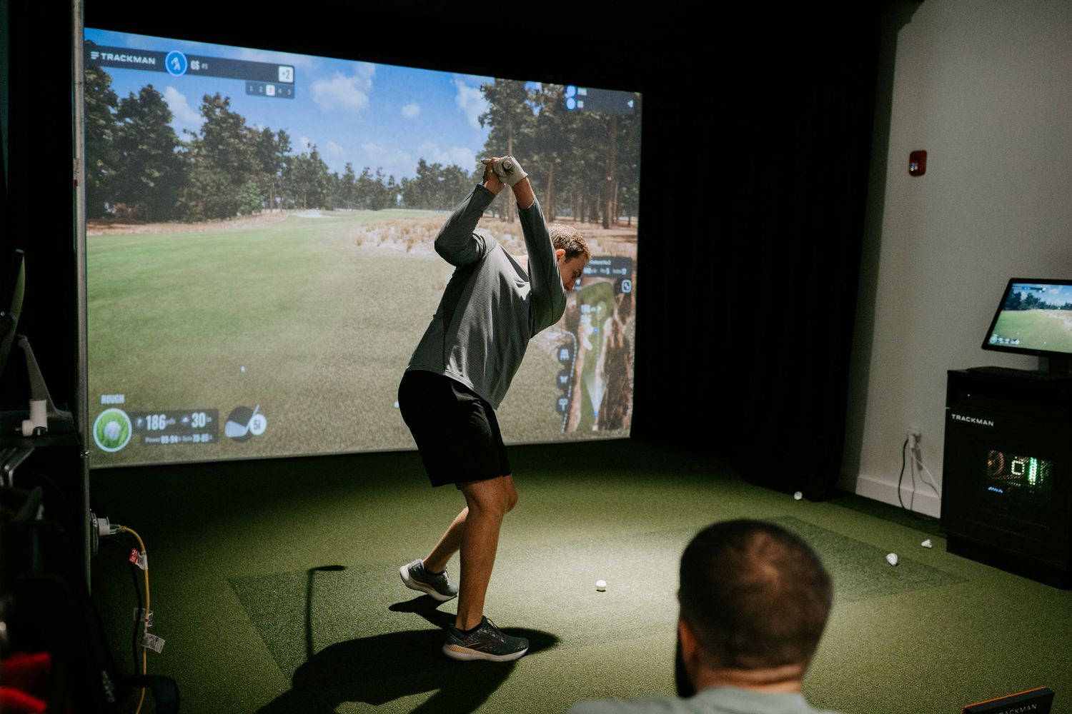 Indoor golf simulator showing a player practicing their swing on a large projected screen.