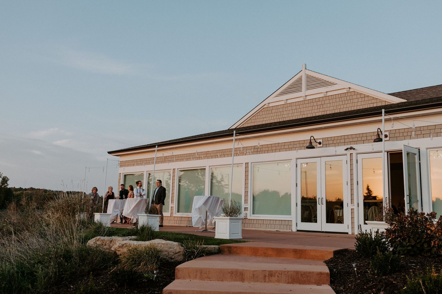Modern wedding venue with glass windows and deck during sunset.