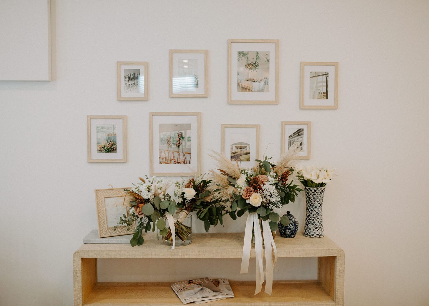 Wedding decor display featuring framed art and floral arrangements on a light wooden table.