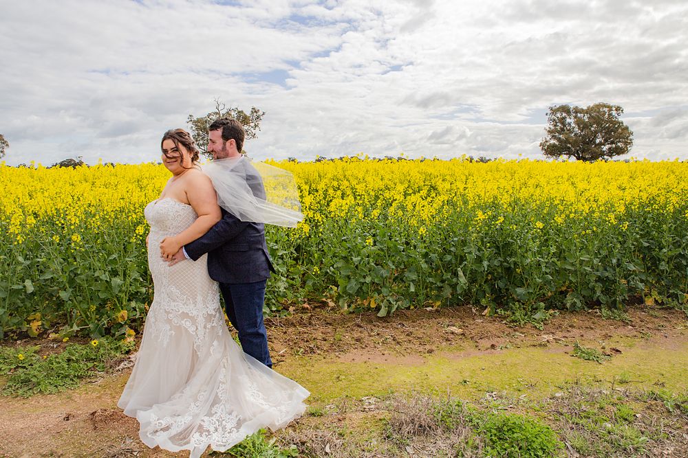 Couple shares intimate wedding moments in a vibrant yellow canola field under cloudy skies.