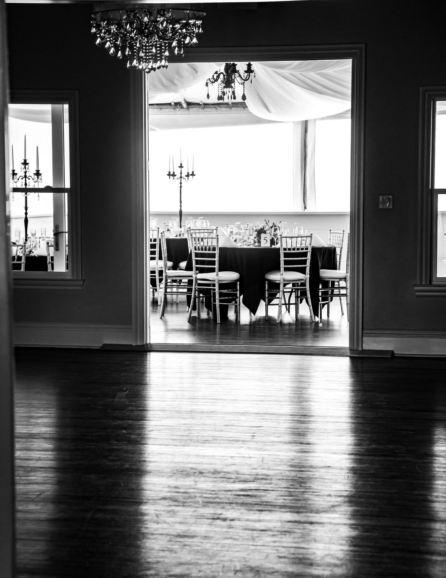 Black and white view of an elegant dining room with chandelier and wooden floors.