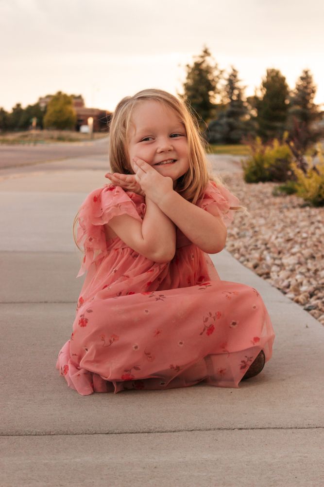Westminster family photographer captures little girl's genuine smile and sweet pose in pink floral dress at sunset
