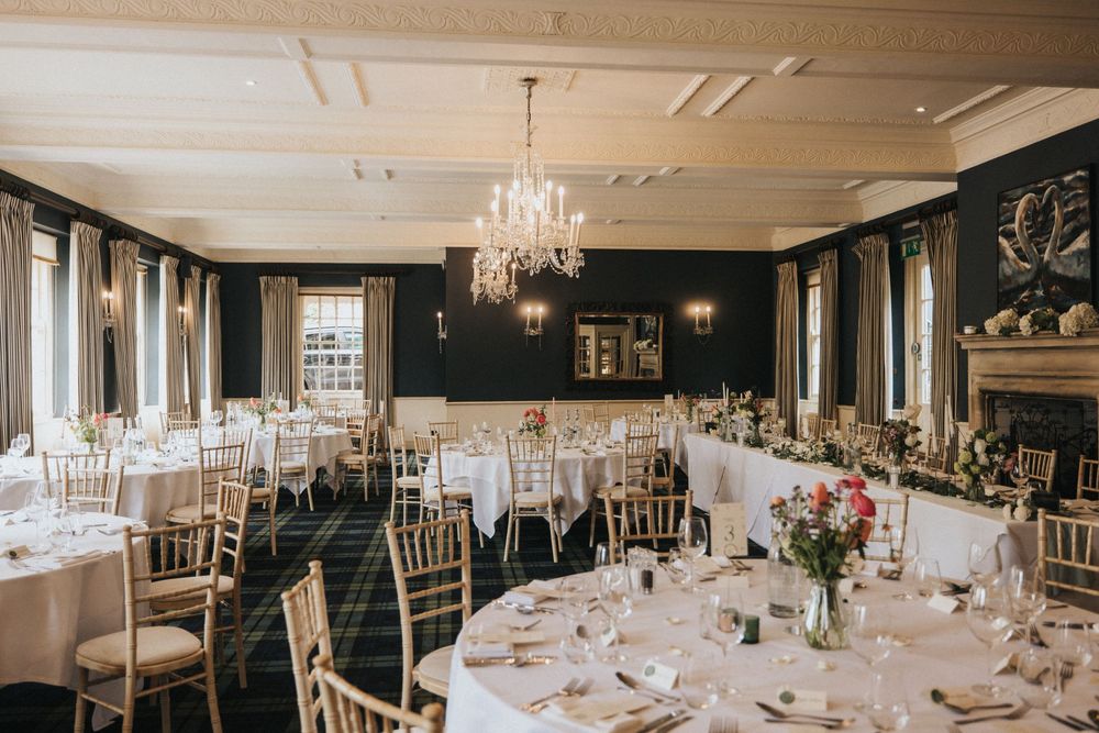 Elegant wedding reception ballroom with crystal chandeliers, white tablecloths and gold chiavari chairs set for celebration.