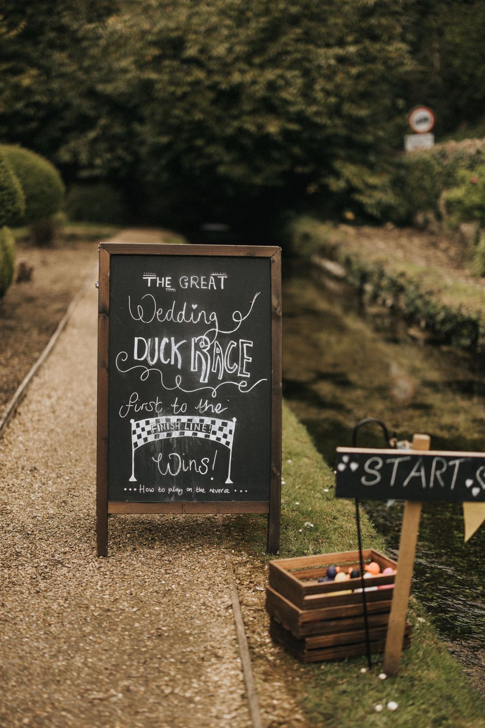 A rustic chalkboard wedding sign and wooden crate decorate a garden path with directional arrows.
