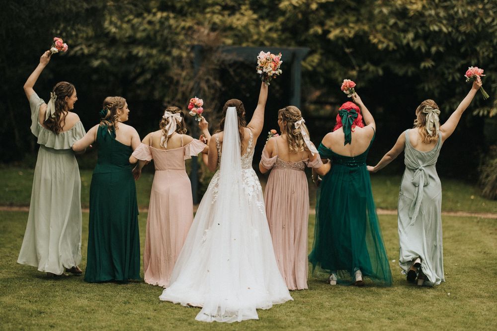 Wedding party dancing on a green lawn in coordinated emerald and blush pink bridesmaid dresses.