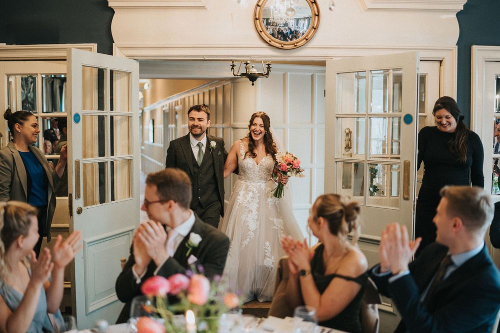 Wedding guests share emotional reactions during ceremony in elegant white trimmed venue with chandeliers.