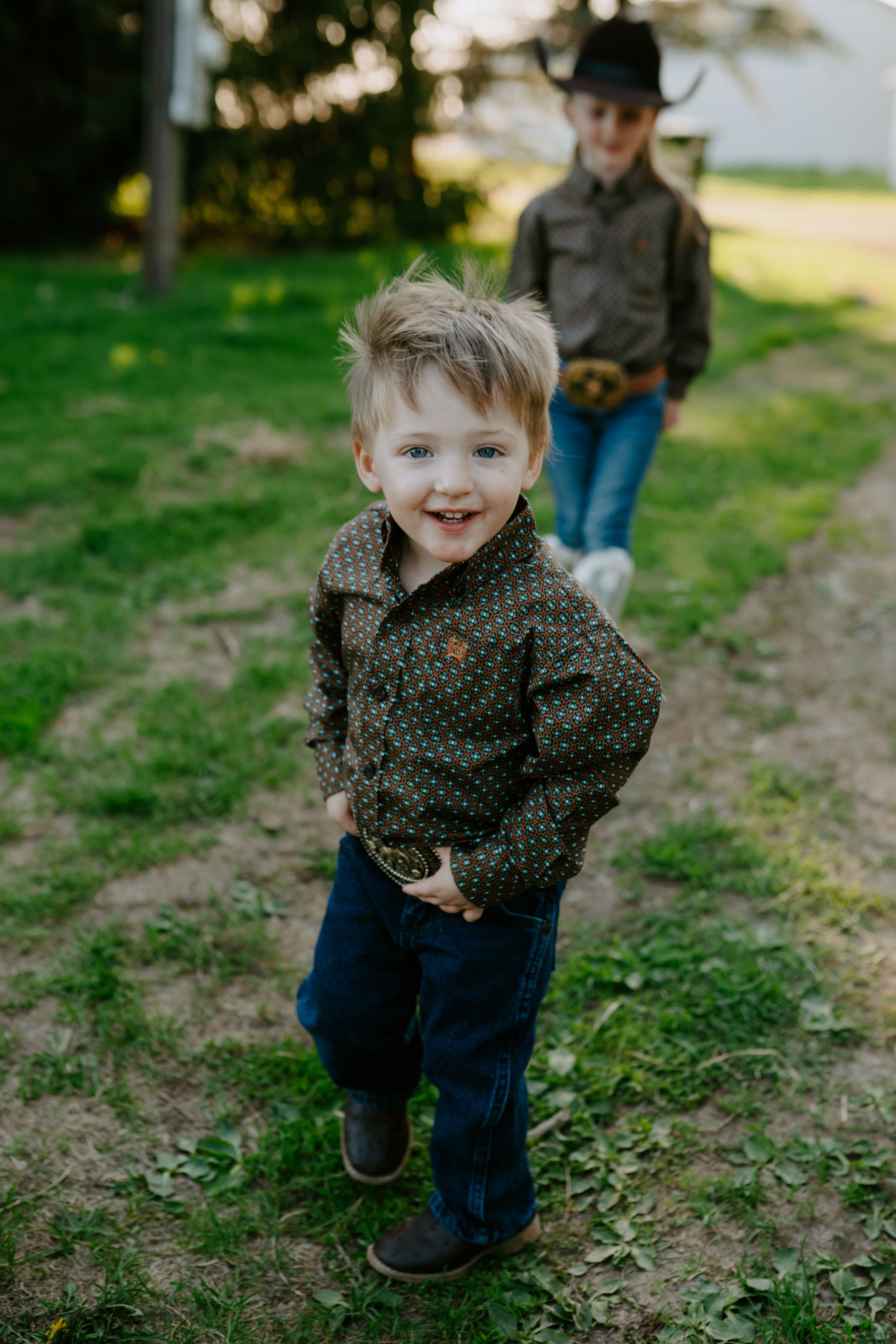 Child in patterned shirt and jeans playing outdoors in a grassy area.