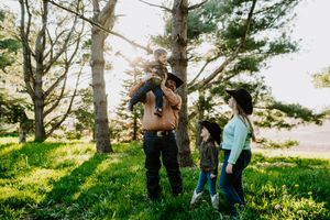 A candid family photo taken in a sun-dappled forest setting with western attire.