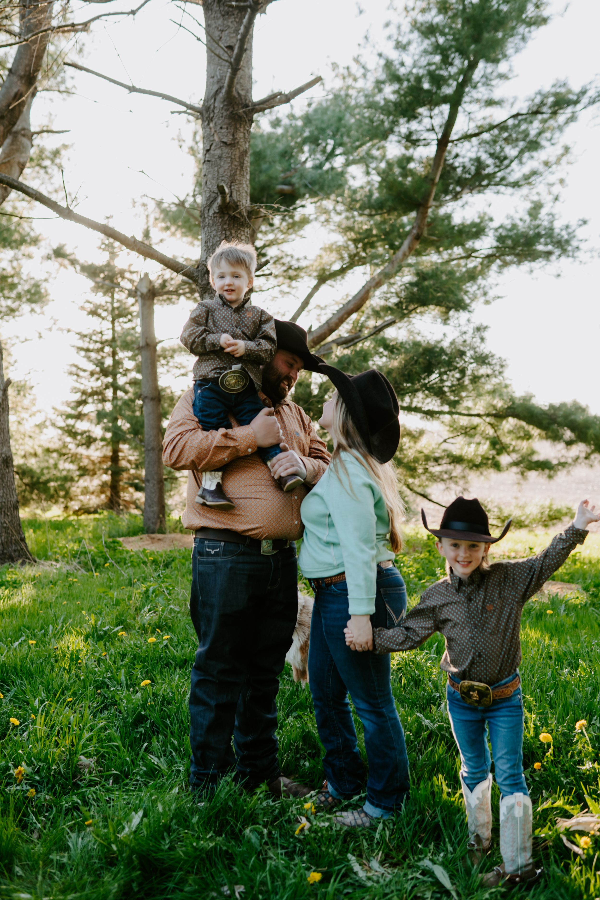 A playful family moment captured outdoors with everyone in western-themed clothing.