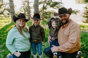 A western-style family portrait with cowboy hats and casual attire sitting together outdoors with their dog.