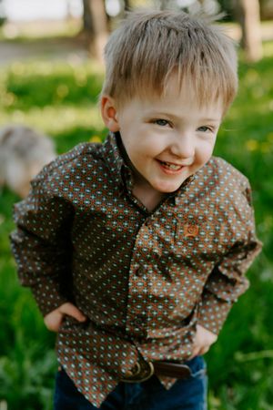 A cheerful child in a patterned shirt poses outdoors with a bright smile.