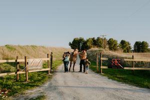 A group walks along a fenced country path with rolling hills in the background.