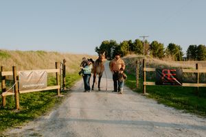 A family strolls down a dirt road between wooden fences on a clear day.