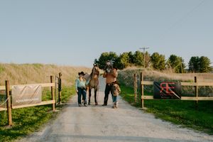 People walking together on a rural path with wooden fencing and hills in the distance.