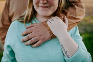 Close-up of hands embracing showing a ring and tattoo against a mint green sweater.
