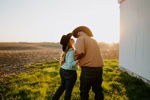 Two people stand together in a field of wildflowers at golden hour.