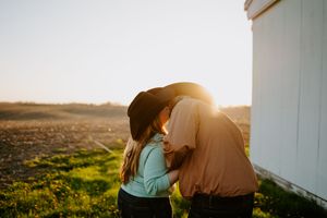 Two figures embrace while standing in a meadow during sunset.