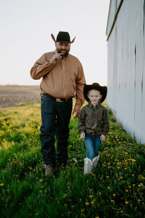 Two people in western wear explore a meadow of yellow wildflowers together.